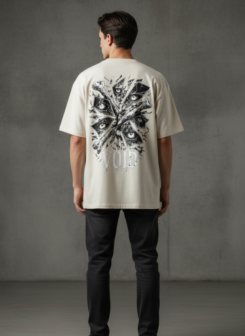 A person with curly hair wears a black T-shirt with crossed bones, eyes in triangles, and the word VOID printed in white on the back. They stand facing away with one hand in their jeans pocket.